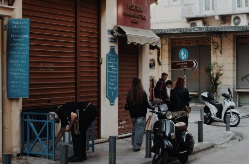 A lively Athens street captures pedestrians, scooters, and shops in the evening light.